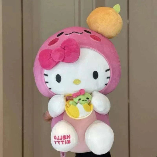 Hello Kitty plushie: pink hood with bow, white face, tan headpiece, holding small charm